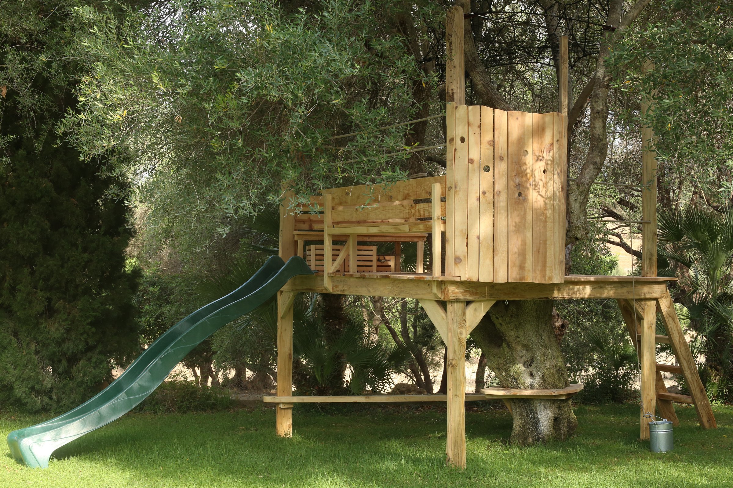 Casa de árbol en Mallorca con tobogán y escalera, rodeada de vegetación mediterránea